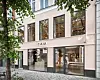 En lys butikkfasade med skiltet CAIA, store vinduer og trær som delvis rammer inn bygningen.