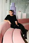 Person sitter på en rosa, bølget sofa i et lyst butikklokale med store rosa og lilla dekorobjekter i bakgrunnen.