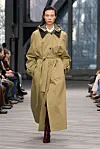 En modell viser en lang, oversized trenchcoat i beige på catwalken til Calvin Klein.
