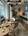 Lyse lokaler med små bord, barkrakker, hengelamper, planter og dempet lys ved vinduet.