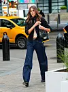 En kvinne går på fortauet i New York, iført svart topp, mørk jeans og svart veske, med en gul taxi i bakgrunnen.
