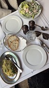 Restaurantbord med hvite tallerkener, salat, brød, bestikk, glass og flere serverte retter.