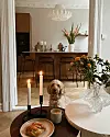 Lys spisestue med tente stearinlys, blomster, frokost på bordet og en liten hund på gulvet.