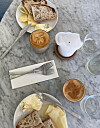 To tallerkener med brød og ost, kaffe, melk, vann og bestikk på et marmorbord.
