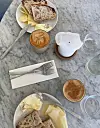 To tallerkener med brød og ost, kaffe, melk, vann og bestikk på et marmorbord.