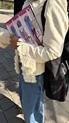 Person i blå jeans og lys frynsejakke holder flere rosa ELLE-magasiner.