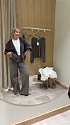 Kvinne i grå jeans og mørk cardigan står foran et speil i et prøverom.
