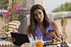 Eva Longoria som Isolde sitter utendørs med nettbrett, mobiltelefon, mat og drikke.