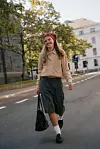 Person i beige jakke, mørkt skjørt og rødt hodeplagg går på en bygates.