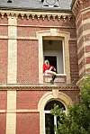 En person i rødt antrekk sitter i et vindu på en utsmykket rød murbygning.
