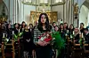 En kvinne holder en blomsterbukett i en kirke, omgitt av mennesker og grønne planter.