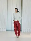 Modell i rød bukse og hvit skjorte går i et lyst, minimalistisk rom.