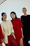 Tre modeller står på en catwalk i antrekk i rødt, kremhvitt og sort.