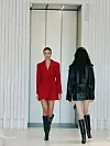 To modeller går gjennom en lys catwalk, iført en rød blazerjakkekjole og et svart skinnantrekk.