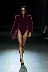Modell i burgunder body, veske, solbriller og pumps går på en opplyst catwalk.