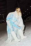 Modell i voluminøst hvitt og lyseblått antrekk på en catwalk i en stor industrihall.