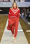 Modell i rødt antrekk går på en catwalk foran sittende publikum.