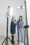 To kvinner står i et lyst studio med mikrofoner, kameraer og studiobelysning.