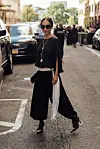 Person i svart antrekk og solbriller står i en bygaten i New York med et lyst, frynsete tilbehør.
