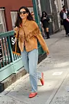Person med brun jakke med frynser, lyse jeans og røde sko går på et fortau i New York.