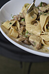 Kremet sopppasta med urter på en hvit tallerken, løftet med en gaffel.