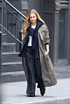 Kvinne går på et fortau i New York iført lang grå trenchcoat, mørke vide bukser og lag på lag.