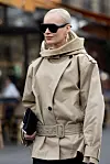 Person i beige trenchcoat med belte og sorte solbriller står på en travel gate.