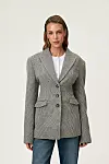 Modell iført grå ullblazer, hvit topp og blå jeans mot lys bakgrunn.