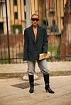 Person i sort oversized blazer, grå bukser og høye sorte boots på en bygaten.