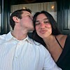 Et par sitter tett sammen innendørs; mannen kysser kvinnen på kinnet mens hun smiler til kameraet.