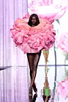 Modell går på en speilblank catwalk i en stor, rosa blomsterkreasjon.
